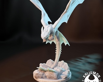 May include: A light grey 3D-printed dragon figurine with outstretched wings, perched on a rocky base. The dragon has detailed scales and a long, segmented tail. The base is a circular platform. The logo "KAIJUMON MINIS" is visible.