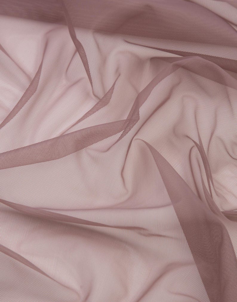 May include: A sheer, lightweight fabric in a dusty mauve or muted rose colour. The material features a fine, semi-transparent mesh texture with soft, flowing folds and drapes that create varying depths of colour across the surface.
