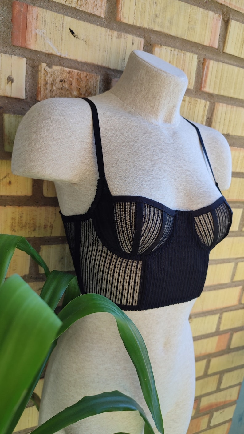 May include: A black mesh and ribbed crop top with thin straps. The top has a sweetheart neckline and a fitted silhouette.