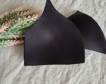 May include: Two black bra cups made of soft, smooth fabric. The cups are shaped like a triangle and have a pointed top.