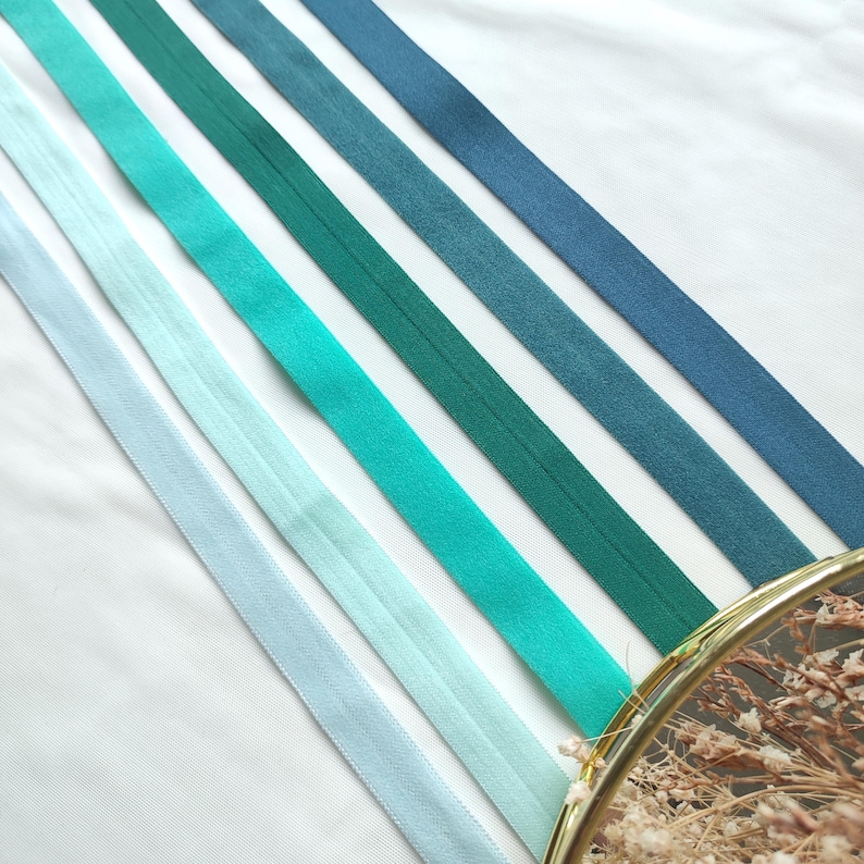 May include: Five different shades of blue and green elastic ribbon. The ribbon is arranged in a diagonal pattern on a white background.