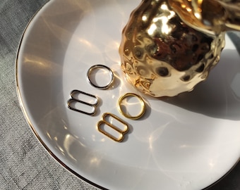 May include: Four metal rings in a variety of sizes and finishes. Two gold rings are in the shape of a figure eight. One silver ring is a simple circle. The fourth ring is a gold circle.