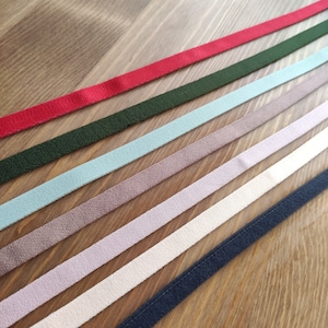 May include: Assortment of seven different colored ribbon trims, including red, green, light blue, brown, pink, white, and navy blue. The ribbons are arranged in a diagonal pattern on a wooden surface.