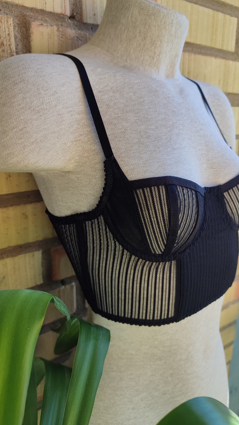 May include: Black lingerie top with a striped mesh design and a black satin trim. The top has adjustable straps and a hook and eye closure in the back.