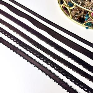 Peut inclure: Divers rubans et élastiques noirs de différentes textures et motifs. Certains ont des bords festonnés, d'autres sont lisses ou côtelés. Les rubans sont disposés en diagonale sur un fond blanc, avec un panier doré de fleurs séchées en arrière-plan.