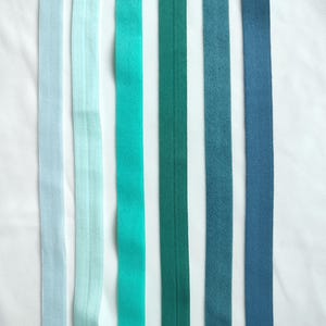 May include: Six different colored ribbon trims in shades of blue and green. The ribbons are arranged vertically and are all the same width.