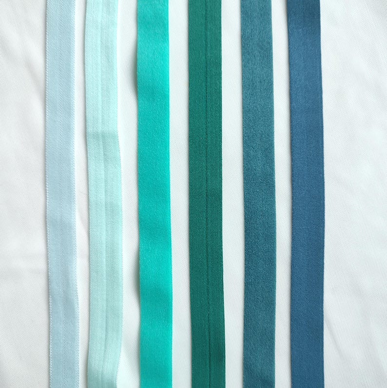 May include: Six different colored ribbon trims in shades of blue and green. The ribbons are arranged vertically and are all the same width.