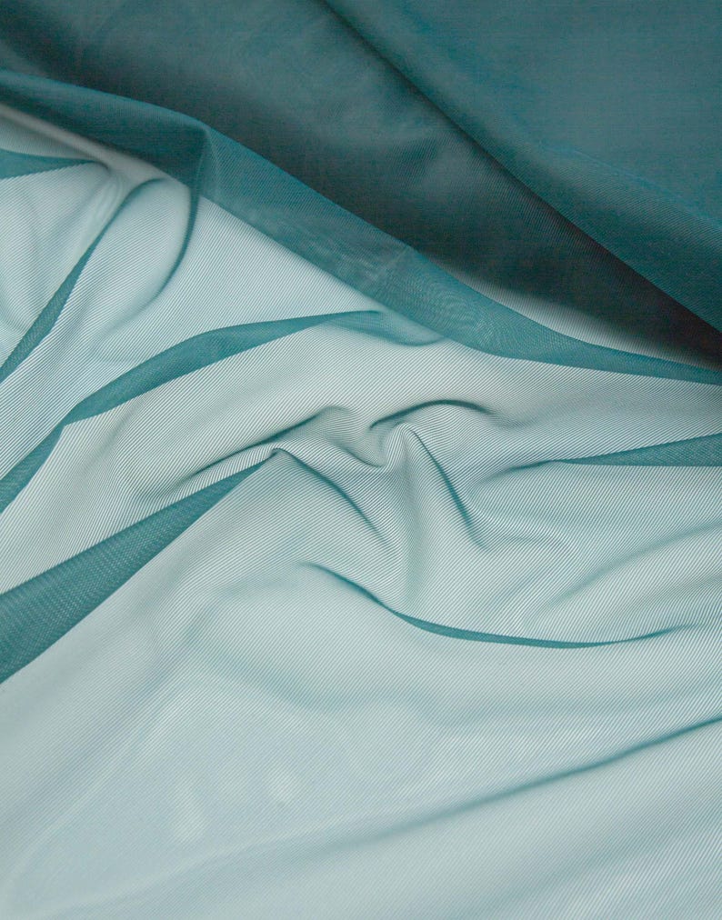 May include: A sheer, lightweight fabric in a deep teal colour, featuring a fine mesh texture. The material is draped in soft, flowing folds, creating varying levels of transparency and depth across the surface of the textile.