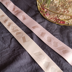 May include: Two pink and beige elastic ribbon trims with the word "PASSION" printed in a contrasting colour on each.