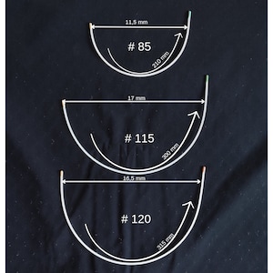 Puede incluir: Tres aros de plástico blanco de diferentes tamaños con medidas en milímetros. Los aros están etiquetados como #85, #115 y #120.