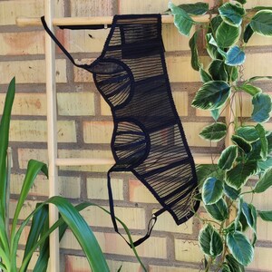 May include: Black sheer lingerie top with a geometric design. The top is hanging on a wooden ladder against a brick wall.