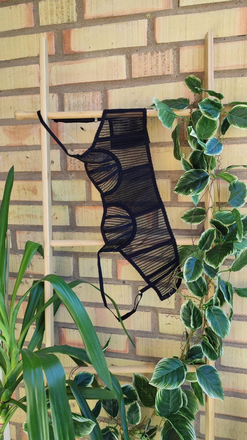May include: Black sheer lingerie top with a geometric design. The top is hanging on a wooden ladder against a brick wall.