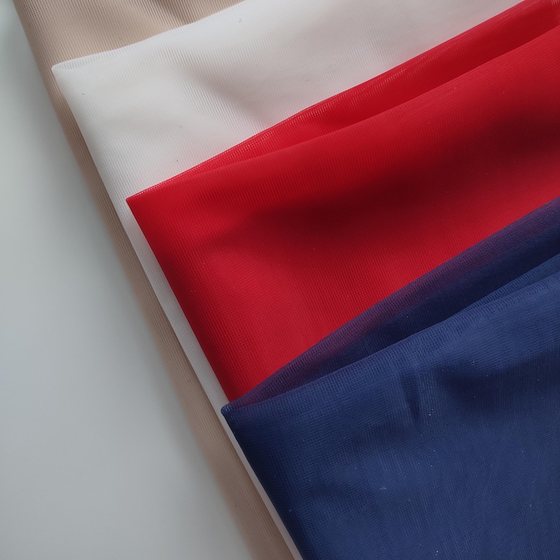 May include: Four layers of sheer, fine-mesh fabric stacked diagonally. The colours from top to bottom are beige, white, bright red, and deep navy blue. Each piece of fabric displays a consistent, semi-transparent, and lightweight texture.