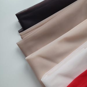 May include: A collection of layered sheer mesh fabric sheets in a gradient of colours, including black, light beige, tan, white, and a vibrant red. Each piece of fabric features a fine, uniform grid texture and a semi-transparent finish.