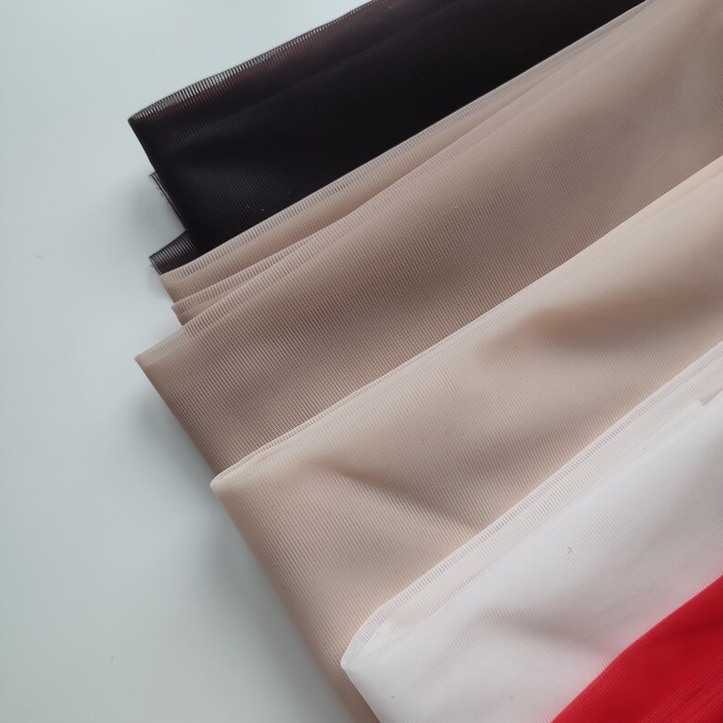 May include: A collection of layered sheer mesh fabric sheets in a gradient of colours, including black, light beige, tan, white, and a vibrant red. Each piece of fabric features a fine, uniform grid texture and a semi-transparent finish.
