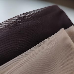 May include: Two layers of fine, semi-sheer mesh fabric are stacked together. The top layer is a deep, dark brown, while the bottom layer is a light, neutral beige. The material features a consistent, small-scale grid pattern throughout.