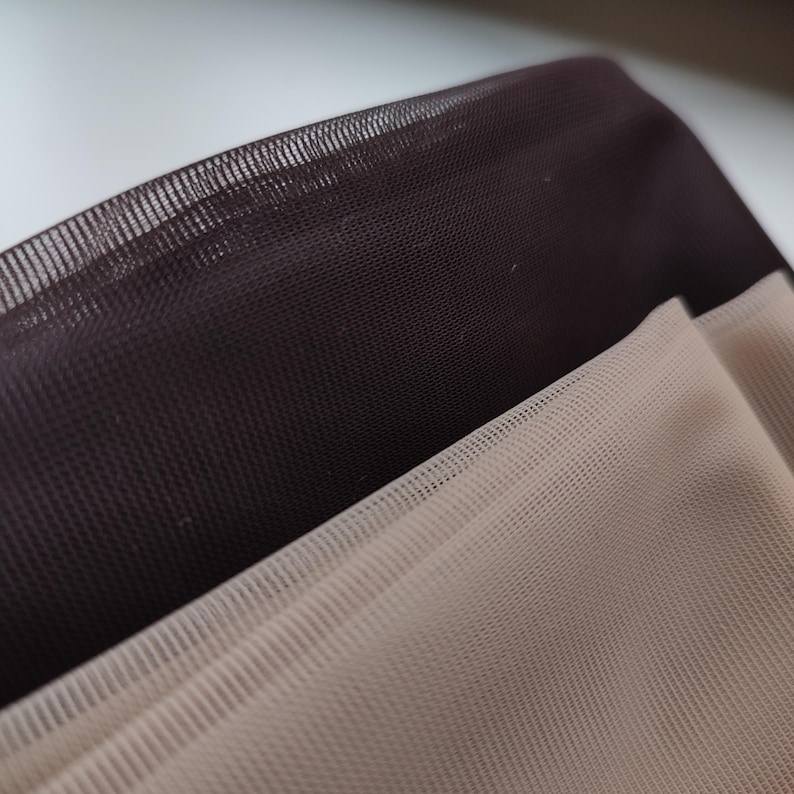 May include: Two layers of fine, semi-sheer mesh fabric are stacked together. The top layer is a deep, dark brown, while the bottom layer is a light, neutral beige. The material features a consistent, small-scale grid pattern throughout.