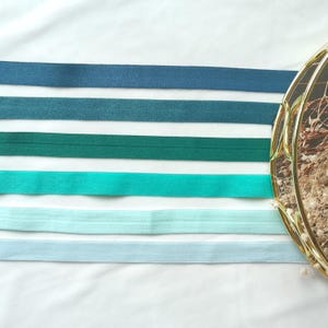 May include: Five different colors of elastic ribbon, from dark blue to light blue, arranged in a horizontal line on a white surface.