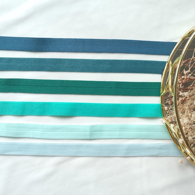 May include: Five different colors of elastic ribbon, from dark blue to light blue, arranged in a horizontal line on a white surface.