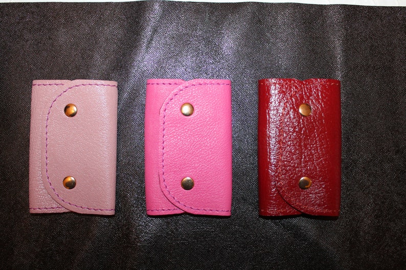 May include: Three leather keychains in different colors: pink, red, and light purple. Each keychain has two gold metal snaps.