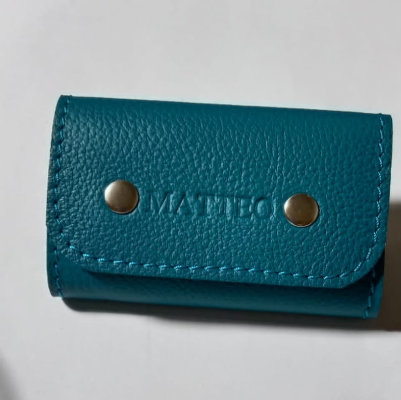 May include: Teal leather key holder with silver snaps and the word "MATTEO" embossed on the front.