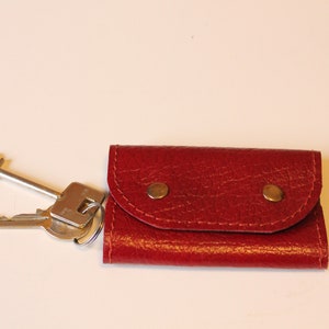 May include: A red leather key holder with two brass snaps. The key holder is closed and has a set of keys attached to it.