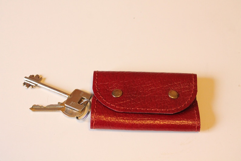 May include: A red leather key holder with two brass snaps. The key holder is closed and has a set of keys attached to it.