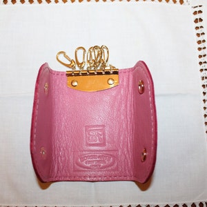 May include: A pink leather key holder with a gold metal key ring and a small metal plate with the text "Genuine Leather" on it.