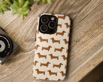 Könnte beinhalten: Eine Handyhülle mit einem sich wiederholenden Muster aus braunen Dackel-Hunden auf cremefarbenem Hintergrund. Die Hülle liegt auf einer Holzoberfläche. Das Telefon hat eine Kamera mit mehreren Objektiven.
