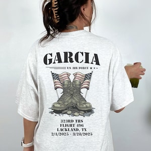 May include: Ash grey t-shirt with a graphic print of military boots and American flags. The text "GARCIA US AIR FORCE" is printed above the graphic. The text "323RD TRS FLIGHT 496 LACKLAND, TX 2/1/2025-3/28/2025" is printed below the graphic.