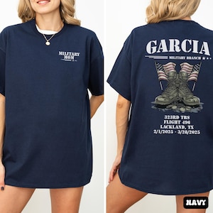 May include: A navy blue t-shirt with the text "MILITARY MOM" on the front and "GARCIA MILITARY BRANCH*** 323RD TRS FLIGHT 496 LACKLAND, TX 2/1/2025-3/28/2025 NAVY" on the back. The back of the shirt also features a graphic of military boots and American flags.