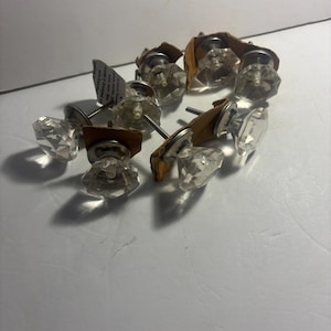 May include: A collection of clear, faceted crystal cabinet knobs with silver-toned bases and long screws. Some knobs are attached to small, brown cardboard squares. The knobs are arranged on a white surface.