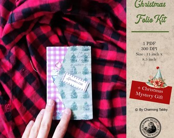 May include: A Christmas folio kit with a red and white checkered background. The kit includes a PDF file with a design for a folio, measuring 11 inches by 8.5 inches, and a mystery gift. The text "December 25th" is visible on the folio.