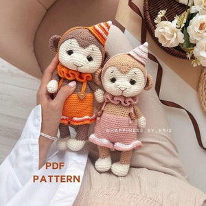 Puede incluir: Dos muñecos de mono de ganchillo hechos a mano. Un mono viste un atuendo naranja y el otro un atuendo rosa. Ambos monos tienen pelaje marrón, caras blancas y gorros de fiesta. El texto "PDF PATTERN" es visible.