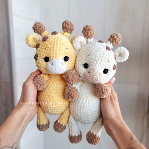 May include: Two crocheted giraffe stuffed animals. One is yellow with brown spots and the other is white with brown spots. Both have brown ears and brown hooves.