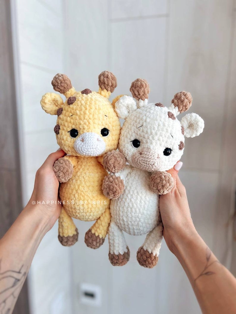 May include: Two crocheted giraffe stuffed animals. One is yellow with brown spots and the other is white with brown spots. Both have brown ears and brown hooves.