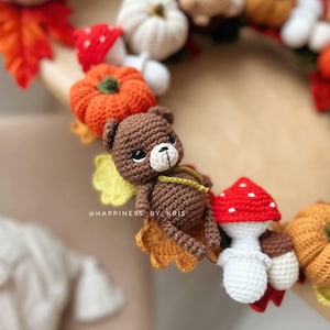 K&ouml;nnte beinhalten: Ein handgefertigter H&auml;kelkranz mit herbstlichen Elementen. Der Kranz enth&auml;lt einen braunen Teddyb&auml;ren, orangefarbene K&uuml;rbisse, wei&szlig;e Pilze mit roten Kappen und Herbstbl&auml;tter. Der Text "@HAPPINESS BY KRIS" ist sichtbar.