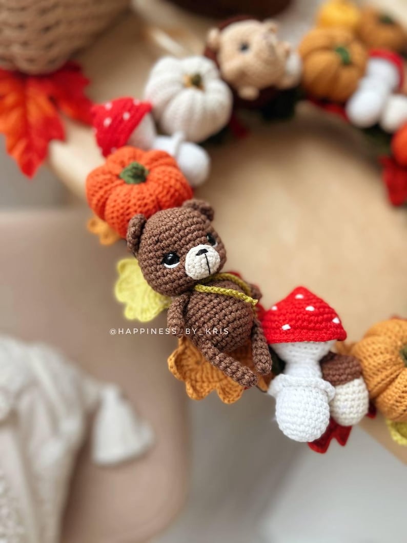 K&ouml;nnte beinhalten: Ein handgefertigter H&auml;kelkranz mit herbstlichen Elementen. Der Kranz enth&auml;lt einen braunen Teddyb&auml;ren, orangefarbene K&uuml;rbisse, wei&szlig;e Pilze mit roten Kappen und Herbstbl&auml;tter. Der Text "@HAPPINESS BY KRIS" ist sichtbar.