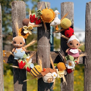 K&ouml;nnte beinhalten: Ein runder Kranz mit verschiedenen geh&auml;kelten Figuren, darunter ein &auml;lteres Paar, eine Biene, eine Ente, ein kleines Haus, Erdbeeren, eine Sonnenblume und Weizen&auml;hren. Der Text "@HAPPINESS_BY_KRIS" ist in der Mitte des Kranzes zu sehen.