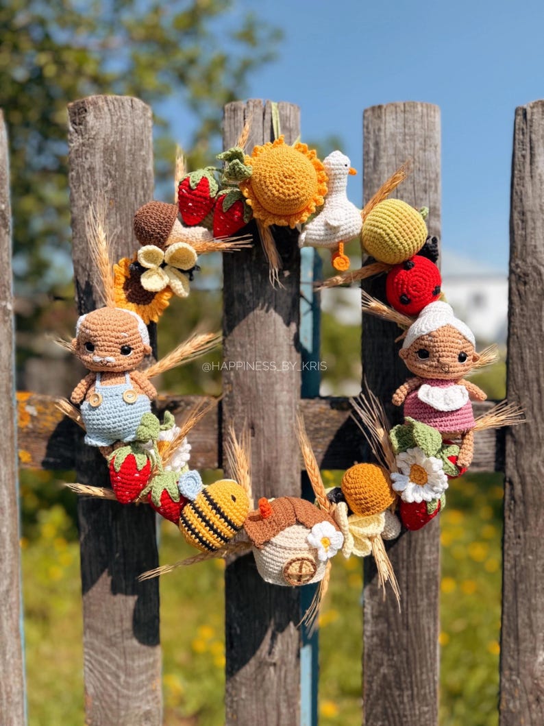 K&ouml;nnte beinhalten: Ein runder Kranz mit verschiedenen geh&auml;kelten Figuren, darunter ein &auml;lteres Paar, eine Biene, eine Ente, ein kleines Haus, Erdbeeren, eine Sonnenblume und Weizen&auml;hren. Der Text "@HAPPINESS_BY_KRIS" ist in der Mitte des Kranzes zu sehen.