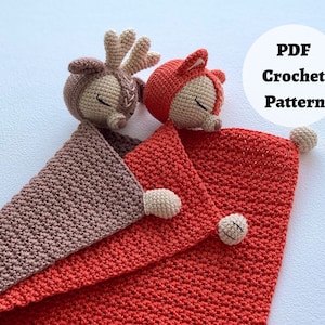Peut inclure: Une couverture b&eacute;b&eacute; en crochet avec un renard et un cerf attach&eacute;s. La couverture est rouge et marron avec une bordure blanche. Le renard est rouge et le cerf est marron. La couverture est faite avec un fil doux et est parfaite pour se blottir.