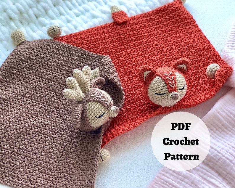 Peut inclure: Deux couvertures pour b&eacute;b&eacute; en crochet avec des applications d'animaux. Une couverture est marron avec une application de cerf et l'autre est orange avec une application de renard. Les couvertures sont dispos&eacute;es sur une surface blanche avec un tissu blanc et rose en arri&egrave;re-plan. Le texte "PDF Crochet Pattern" est visible sur l'image.