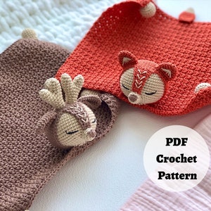 Peut inclure: Deux couvertures pour b&eacute;b&eacute; en crochet avec des applications d'animaux. Une couverture est marron avec une application de cerf et l'autre est orange avec une application de renard. Les couvertures sont sur une surface blanche avec une couverture rose et blanche en arri&egrave;re-plan. Le texte "PDF Crochet Pattern" est sur un cercle blanc.
