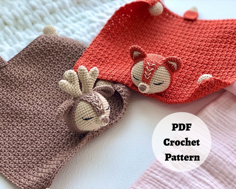 Peut inclure: Deux couvertures pour b&eacute;b&eacute; en crochet avec des applications d'animaux. Une couverture est marron avec une application de cerf et l'autre est orange avec une application de renard. Les couvertures sont sur une surface blanche avec une couverture rose et blanche en arri&egrave;re-plan. Le texte "PDF Crochet Pattern" est sur un cercle blanc.