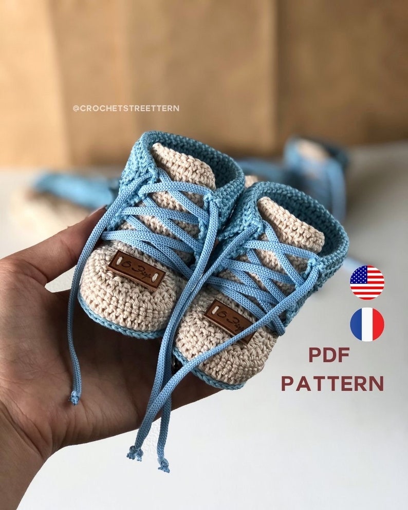 Pode incluir: Um par de sapatos de beb&eacute; de croch&ecirc; em azul e bege com cadar&ccedil;os brancos. Os sapatos t&ecirc;m uma etiqueta de couro castanho com o texto "3-3" neles. PADR&Atilde;O PDF.