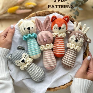 Puede incluir: Colección de cinco sonajeros de bebé hechos a mano con ganchillo en forma de animales, incluyendo un oso, un conejo, un zorro, un ciervo y un lobo. Cada sonajero tiene un cuerpo a rayas y un cuello con volantes. El texto "5 PDF PATTERNS" es visible.