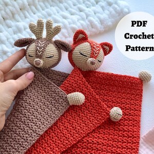 Peut inclure: Une couverture b&eacute;b&eacute; en crochet avec un cerf et un renard attach&eacute;s. La couverture est rouge et marron. Le cerf est marron et le renard est orange. Le texte "PDF Crochet Pattern" est dans un cercle blanc sur fond blanc.