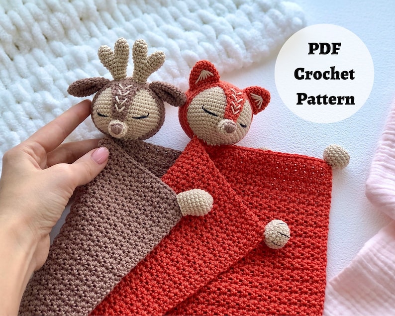 Peut inclure: Une couverture b&eacute;b&eacute; en crochet avec un cerf et un renard attach&eacute;s. La couverture est rouge et marron. Le cerf est marron et le renard est orange. Le texte "PDF Crochet Pattern" est dans un cercle blanc sur fond blanc.