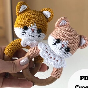 May include: Two crocheted cat toys with wooden rings. One cat is yellow and the other is pink. Both have white crocheted collars.