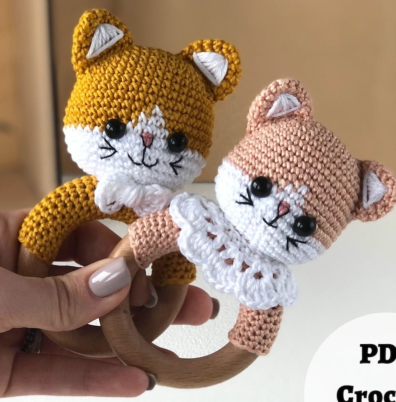 May include: Two crocheted cat toys with wooden rings. One cat is yellow and the other is pink. Both have white crocheted collars.